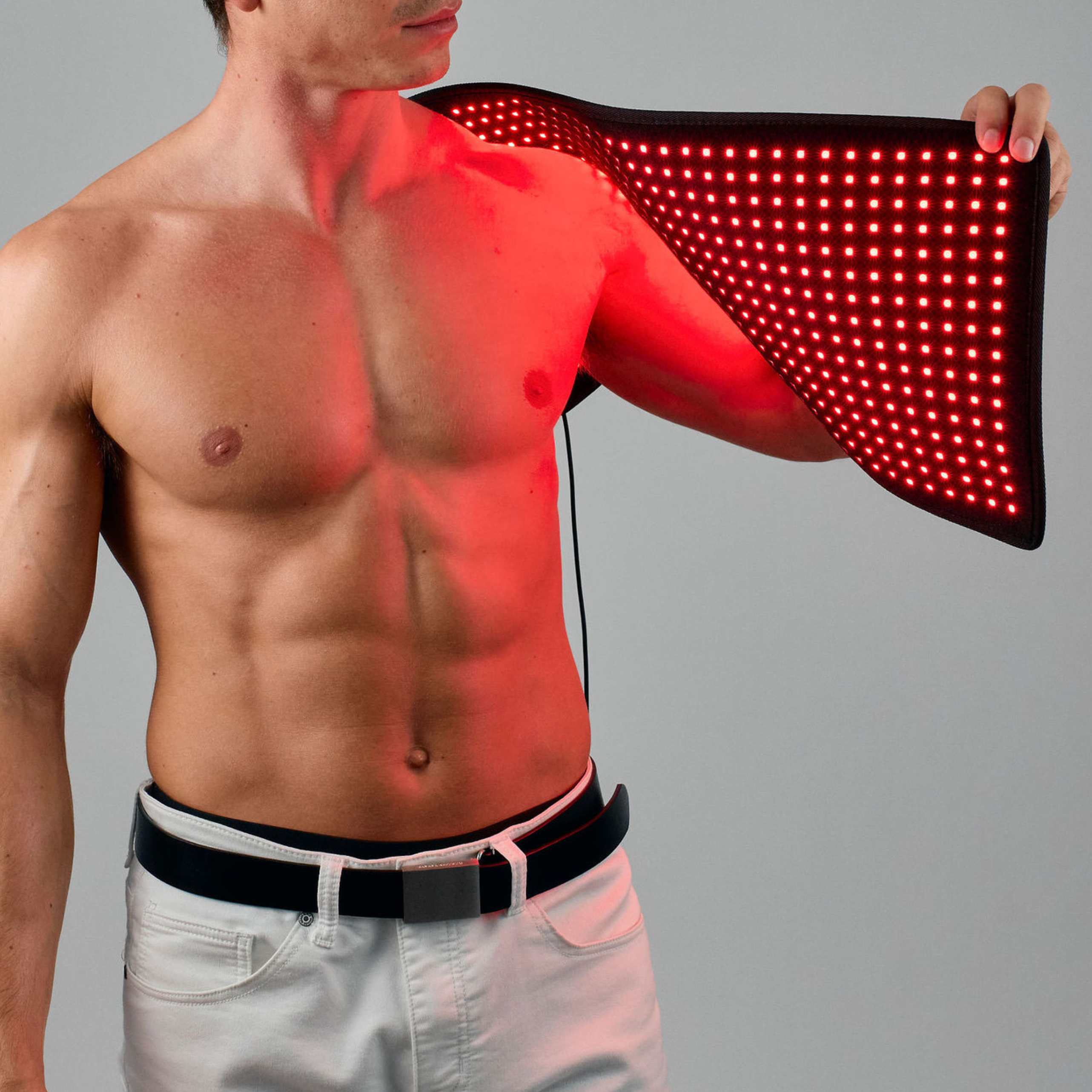 Man applying a red LED therapy pad to his shoulder