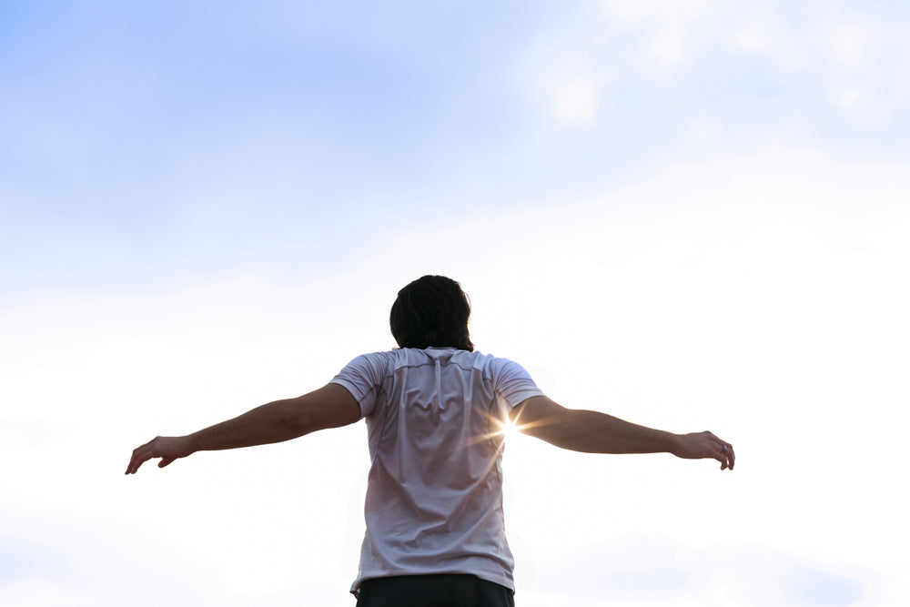 Person standing outdoors with arms outstretched toward the sun